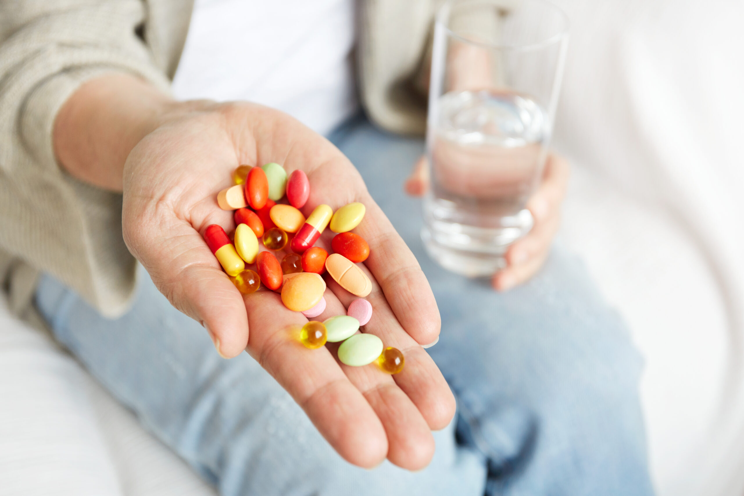 Pills, tablets, vitamins and drugs heap in mature hands, closeup view.